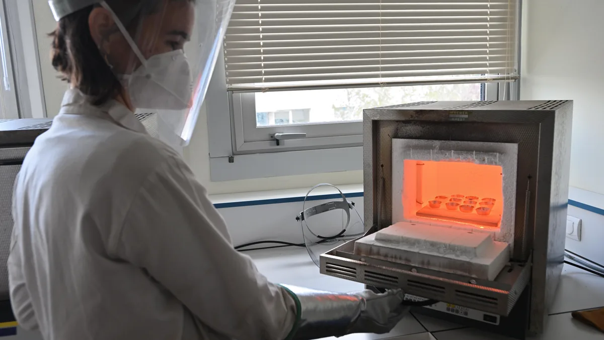 Técnica de laboratorio manipulando muestras de roca en un horno de alta temperatura durante la preparación para XRF